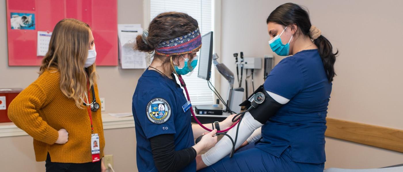 Two U N E health professions students perform a blood pressure exam on a third student in a hospital room